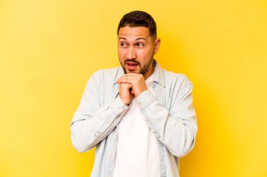 Latin kökenli genç adam sarı arka planda izole edilmiş şans için dua ediyor, şaşırmış ve ağzını açıp önüne bakıyor..