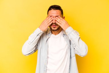 Sarı arka planda izole edilmiş genç İspanyol adam elleriyle gözlerini kapatmaktan korkuyor..