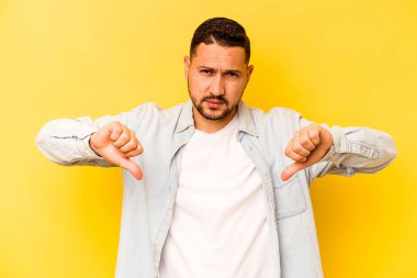 Sarı arka planda izole edilmiş genç İspanyol adam baş parmağını aşağı gösteriyor, hayal kırıklığı konsepti..