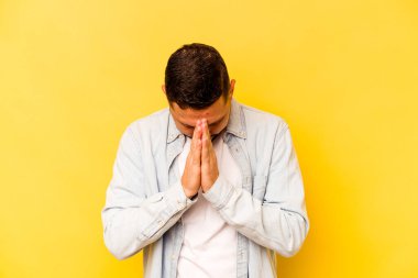 İspanyol asıllı genç adam sarı arka planda izole edilmiş dua ediyor, bağlılık gösteriyor, dindar biri ilahi ilhamı arıyor..