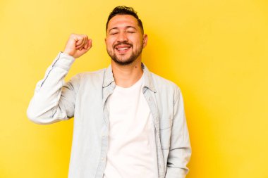 Sarı arka planda izole edilmiş genç İspanyol bir adam zaferi, tutkuyu ve coşkuyu kutluyor, mutlu bir ifade..