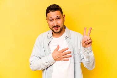Sarı arka planda izole edilmiş genç İspanyol bir adam yemin ediyor, elini göğsüne koyuyor..