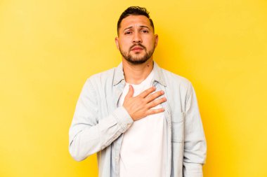 Sarı arka planda izole edilmiş genç İspanyol bir adam yemin ediyor, elini göğsüne koyuyor..