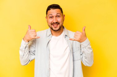 Sarı arka planda izole edilmiş genç bir İspanyol, parmakları olan bir cep telefonu hareketi gösteriyor..