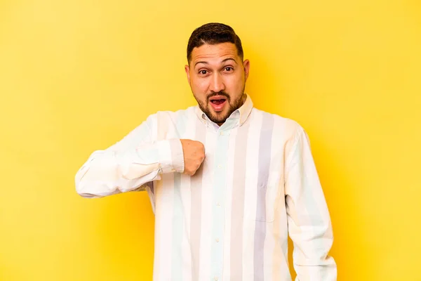 Young hispanic man isolated on yellow background surprised pointing with finger, smiling broadly.
