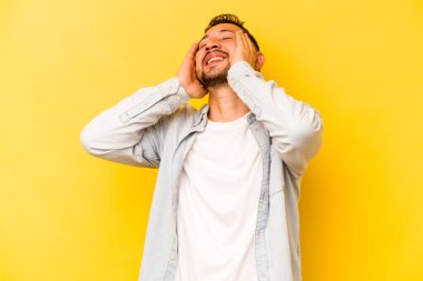 Sarı arka planda izole edilmiş genç İspanyol adam mutlu bir şekilde ellerini başının üstünde tutarak gülüyor. Mutluluk kavramı.