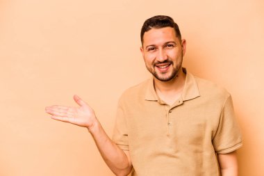 Latin kökenli genç bir adam bej arka planda izole edilmiş. Bir avuç içinde fotokopi alanı ve belinde bir el daha gösteriyor..