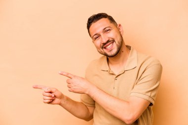 Latin kökenli genç adam bej arka planda izole edilmiş. İşaret parmaklarıyla işaret ettiği için heyecanlı..