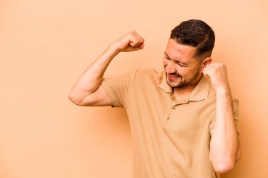 Latin kökenli genç adam bej arka planda izole edilmiş zafer kazandıktan sonra yumruğunu kaldırıyor, kazanan konsept.