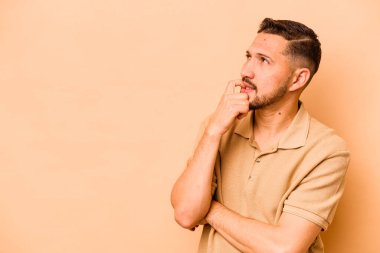 Latin kökenli genç adam bej arka planda izole edilmiş. Rahatlamış bir şekilde fotokopi odasına bakıyor..