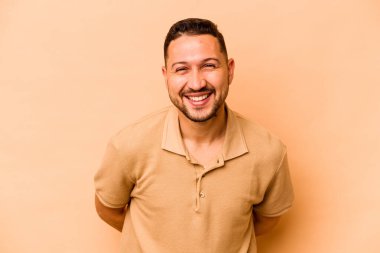 Genç İspanyol adam bej arka planda izole edilmiş mutlu, güler yüzlü ve neşeli.