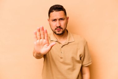 Latin kökenli genç bir adam, bej arka planda izole edilmiş, elini uzatmış, dur işareti göstererek seni engelliyor..