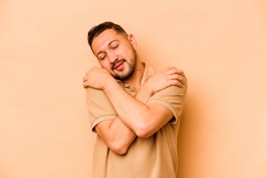 Latin kökenli genç adam bej sarılıp, kaygısız ve mutlu bir şekilde sırıtıyor..