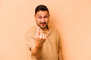 Latin kökenli genç bir adam bej arka planda izole edilmiş. Sanki seni davet ediyormuş gibi seni işaret ediyor..