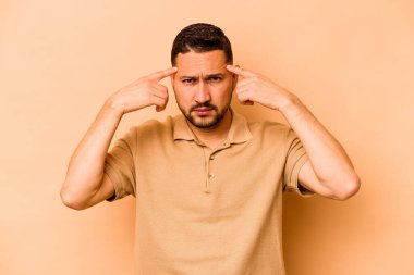 Latin kökenli genç bir adam bej arka planda izole edilmiş bir vazifeye odaklanmış, işaret parmaklarını işaret ediyor..