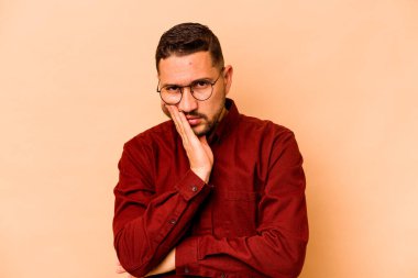 Bej arka planda izole edilmiş, sıkılmış, yorgun ve dinlenmeye ihtiyacı olan genç İspanyol bir adam..