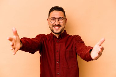 Latin kökenli genç adam bej arka planda izole edilmiş kameraya sarıldığı için kendinden emin..
