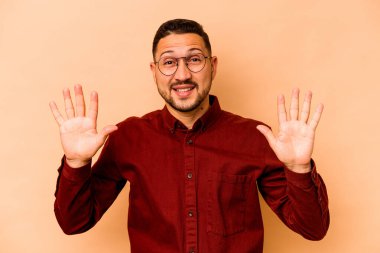 Latin kökenli genç adam bej arka planda izole edilmiş. Elleriyle on numarayı gösteriyor..