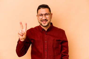 Genç İspanyol adam bej arka planda izole edilmiş neşeli ve kaygısız parmakları olan bir barış sembolü gösteriyor..