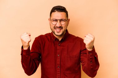 Genç İspanyol adam bej arka planda izole edilmiş tasasız ve heyecanlı tezahüratlar yapıyor. Zafer konsepti.