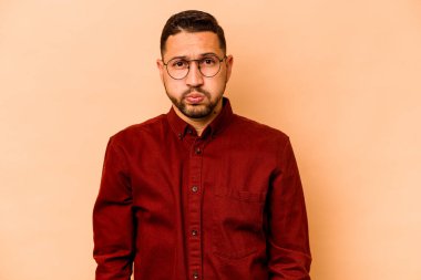 Bej arka planda izole edilmiş genç İspanyol adam yanakları patlatıyor, yorgun bir ifade takınıyor. Yüz ifadesi kavramı.