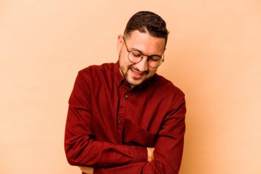 Genç İspanyol adam bej arka planda izole edilmiş gülüyor ve eğleniyor..