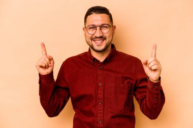 Latin kökenli genç bir adam bej arka planda izole edilmiş. İki parmağı da boş bir alan gösteriyor..