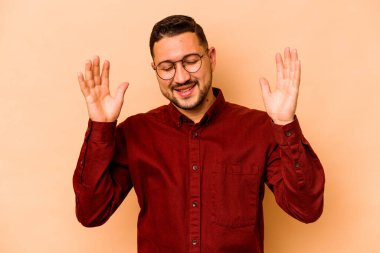 Latin kökenli genç bir adam bej arka planda izole edilmiş neşeli bir şekilde gülüyor. Mutluluk kavramı.