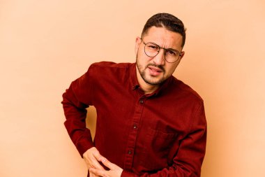 Latin kökenli genç bir adam bej arka planda karaciğer ağrısı ve karın ağrısı çekiyor..