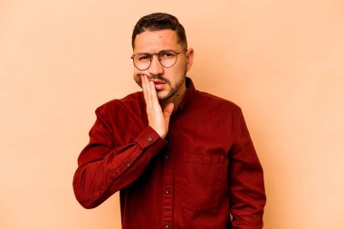 Genç İspanyol adam bej arka planda izole edilmiş güçlü bir diş ağrısı, azıdişi ağrısı var..