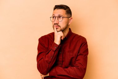 Latin kökenli genç bir adam bej arka planda izole edilmiş. Bir strateji planlıyor, bir iş yolu düşünüyor..