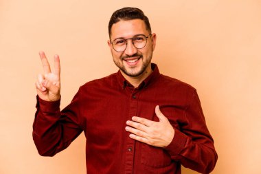 Latin kökenli genç adam bej arka planda izole edilmiş. Yemin ediyor, elini göğsüne koyuyor..