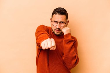 Latin kökenli genç bir adam bej arka planda izole edilmiş. Yumruk atıyor, sinirleniyor, tartışıyor, boks yapıyor..