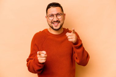 Latin kökenli genç adam bej arka planda izole edilmiş. Parmaklarıyla öne bakıyor..