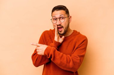 Latin kökenli genç bir adam bej arka planda izole edilmiş. Dedikodu yapıyor, bir şeyleri bildiriyor..