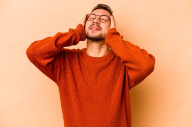 Latin kökenli genç bir adam bej arka planda yalnızken mutlu bir şekilde ellerini başının üstünde tutuyor. Mutluluk kavramı.