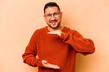 Latin kökenli genç adam bej arka planda iki eliyle bir şey tutuyor, ürün sunumu..