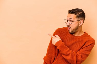 Latin kökenli genç adam bej arka planda izole edilmiş, başparmak uzakta, gülüyor ve kaygısız..