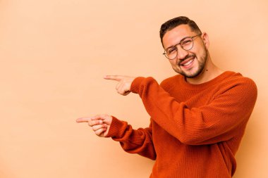 Latin kökenli genç adam bej arka planda izole edilmiş. İşaret parmaklarıyla işaret ettiği için heyecanlı..