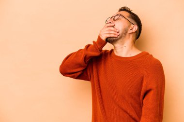 Latin kökenli genç adam bej arka planda izole edilmiş gülerek, kaygısız, doğal duygularla gülüyor..