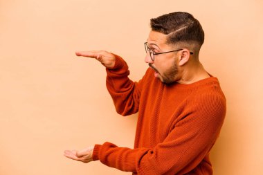 Latin kökenli genç adam bej arka planda izole edilmiş. Elleri arasında bir kopya alanı tutarken şok olmuş ve hayrete düşmüştü..