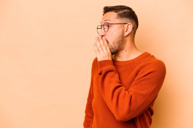 Latin kökenli genç bir adam bej arka planda izole edilmiş. Gördüğü bir şey yüzünden şok oluyor..