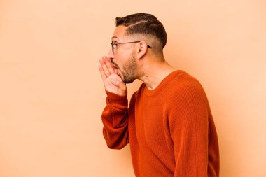 Latin kökenli genç adam, bej arka planda izole edilmiş bir şekilde gizli bir fren haberi veriyor.