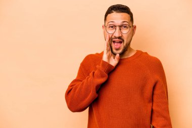 Latin kökenli genç adam bej arka planda izole edilmiş yüksek sesle bağırıyor, gözleri açık ve elleri gergin tutuyor.