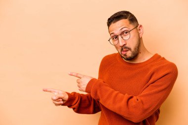 Latin kökenli genç adam bej arka planda izole edilmiş ve işaret parmağıyla fotokopi alanını işaret ederek heyecan ve arzusunu ifade ediyor..