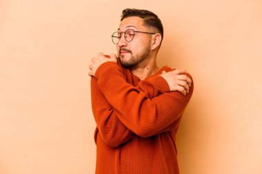 Latin kökenli genç adam bej sarılıp, kaygısız ve mutlu bir şekilde sırıtıyor..