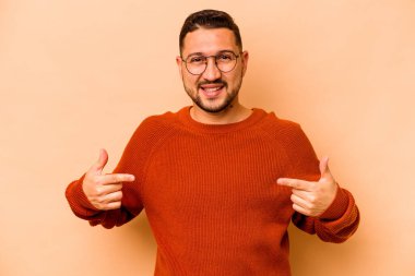 Latin kökenli genç adam bej arka planda izole edilmiş. Parmakları aşağıda, olumlu hisler içinde..