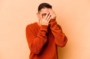 Latin kökenli genç adam bej arka planda izole edilmiş. Korkmuş ve gergin parmaklarıyla göz kırp..