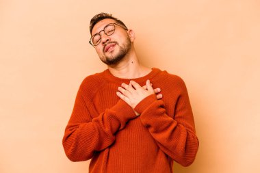 Bej arka planda izole edilmiş genç İspanyol bir adam dost ifadesine sahip, avuçlarını göğsüne bastırıyor. Aşk konsepti.