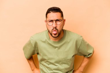 Latin kökenli genç adam, bej arka planda izole edilmiş komik ve dost canlısı bir dil kullanıyor..